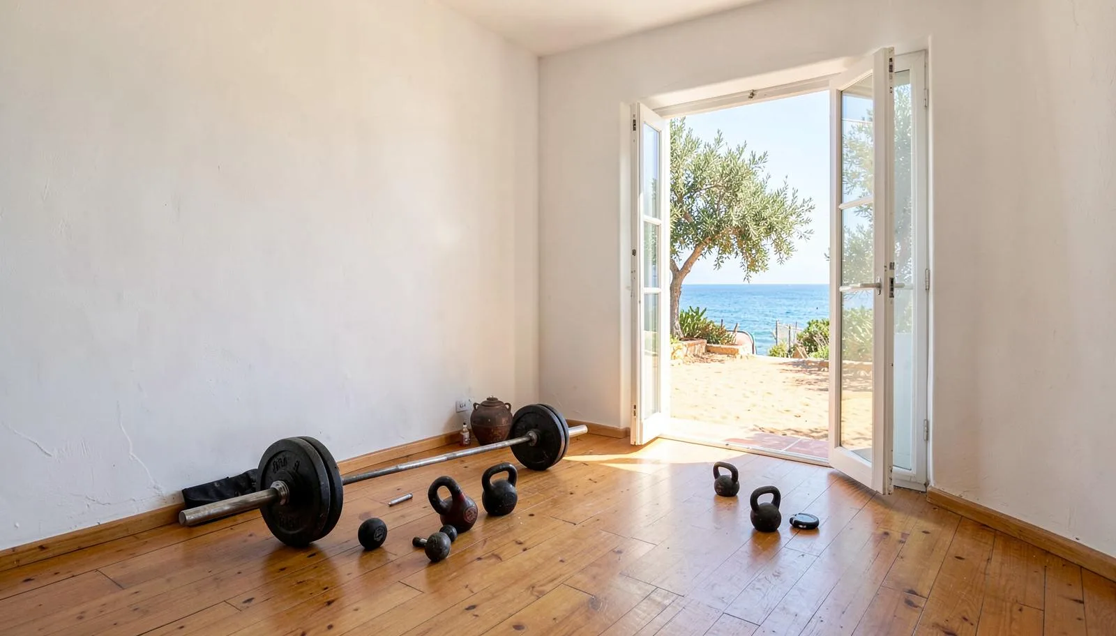 Zasebni vadbeni prostor z olimpijsko palico in kettlebelli ob odprtih vratih na morje